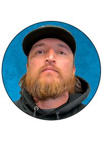 A man with beard and cap is in front of blue background.